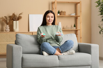 Beautiful young happy Asian woman with contact lens case and eyeglasses sitting on sofa at home