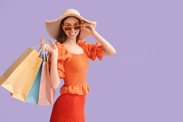 Beautiful young woman with shopping bags on lilac background