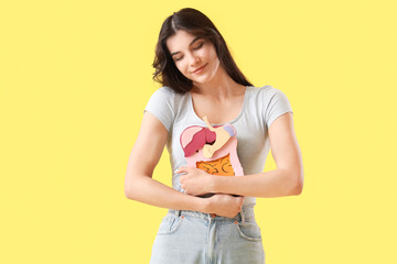 Young woman with paper digestive system on yellow background