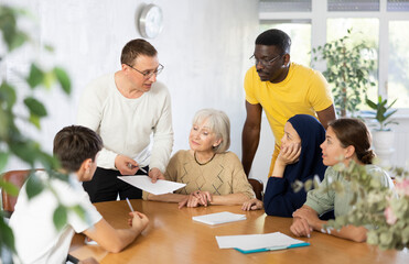 Fototapeta premium Positive adult man participating in work of volunteer group, discussing project or event with associates, men and women of different ages and nationalities gathered around table..