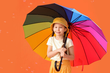 Cute little girl with umbrella and soap bubbles on orange background