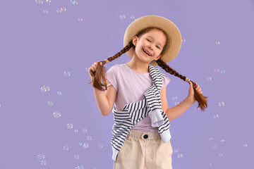 Cute little girl with soap bubbles on lilac background