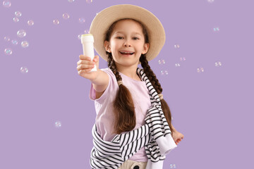 Cute little girl with soap bubbles on lilac background