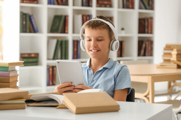 Teenage boy in headphones with tablet computer at library