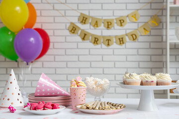 Table with different sweets and decor for birthday party against white brick wall