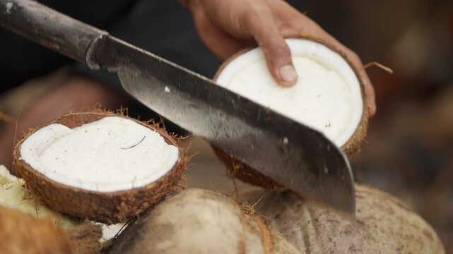 Slow motion, close-up, farmer opening coconut with machete for harvesting meat, copra production