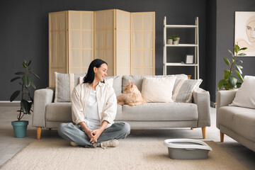 Beautiful young happy woman and cute Maine Coon cat with litter box sitting on floor at home © Pixel-Shot