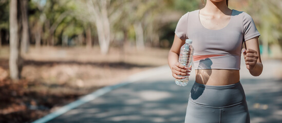 Obraz premium Young woman jogging in park holding water bottle, wearing athletic clothing, enjoying outdoor exercise on sunny day.