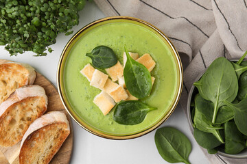 Delicious spinach cream soup with croutons in bowl on white tiled table, flat lay