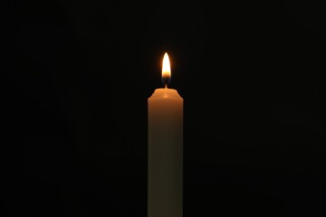 One burning church candle on black background