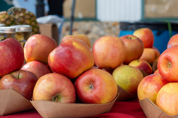 A stack or bulk supply of large red ripe Fuji apples on a table for sale at a farmer's market. The apples are in cardboard trays for sale. The red organic apples are fresh sweet produce.