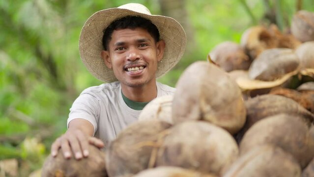 Portrait of young southeast asian farmer, smiling at camera, in straw hat on farm, coconut smallholder in rural asia