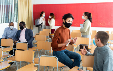 .Viral threat, seasonal viral diseases. Multiethnic group of people in classroom in medical masks, protecting students from viruses