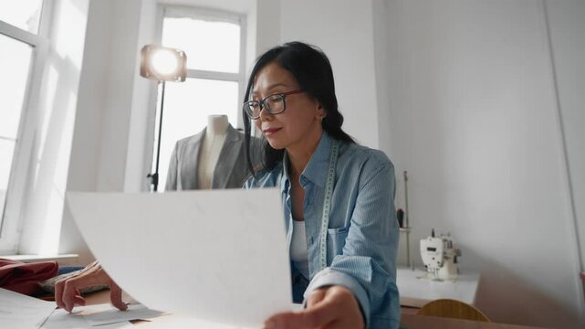 Seamstress woman viewing sketches and patterns in atelier, fashion business. Portrait of professional female designer of clothes working in her own studio, modern tailor-made atelier, creative hobby