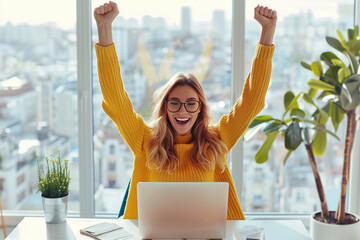 A joyful woman sitting at her desk, raising both hands in the air with joy