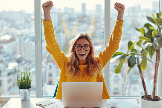 A joyful woman sitting at her desk, raising both hands in the air with joy