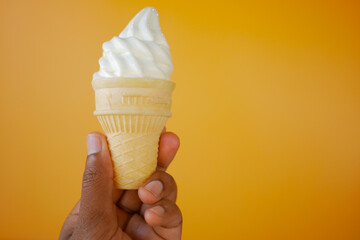 Hand Holding Vanilla Soft Serve Ice Cream Cone against Vibrant Orange Background