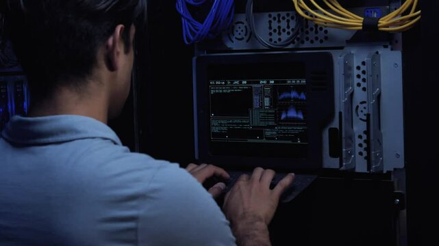 IT Engineer Enters Information Using a Flat Keyboard on Modern Screen Interface. Inside Secure Server Room.  Data Center. Close Up. Engineer over Shoulder. 