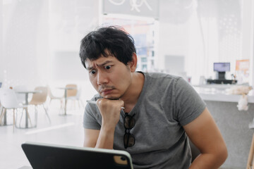 Unhappy asian Thai man focused working on laptop in cafe, get stressed and confusing, have no idea. 