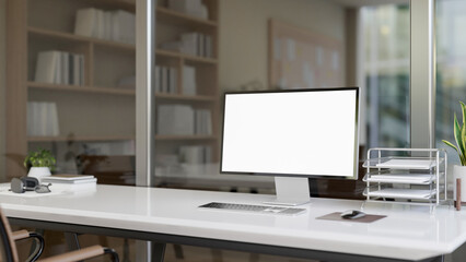 A computer desk in a modern office features a computer with white-screen mockup and office supplies.