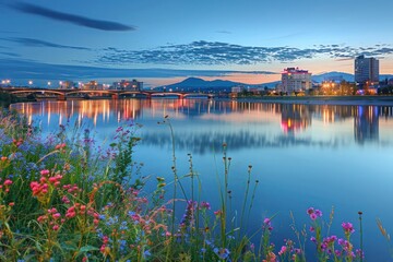 A city waterfront at dusk, with the skyline reflecting in the water and illuminated bridges crossing busy channels. On the other side, a calm rural riverbank at dawn