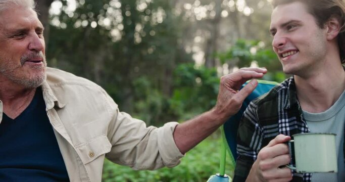 Camping, man and father toast in nature on outdoor holiday vacation for chat, family and natural forest. Talking, coffee and senior dad drinking with happy son on adventure in Australia and woods