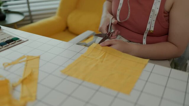 designer is cutting fabric according to the pattern the customer wants, a tailor cuts large pieces of cloth that has been measured to the desired size in oder to make a garment