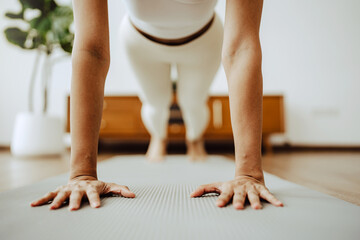 Young Asian woman in sportswear doing plank on training mat while watching online workout tutorials on laptop in the living room. Sport and recreation concept