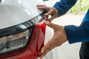 A businessman stands next to his damaged vehicle after an accident, holding a clipboard and...