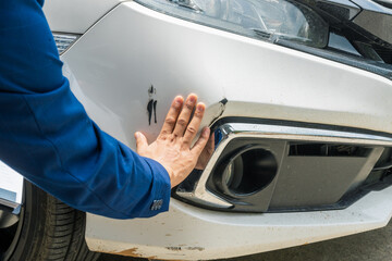 A businessman stands next to his damaged vehicle after an accident, holding a clipboard and...