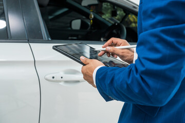 A businessman stands next to his damaged vehicle after an accident, holding a clipboard and...