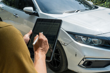 A businessman stands next to his damaged vehicle after an accident, holding a clipboard and...