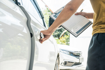 A businessman stands next to his damaged vehicle after an accident, holding a clipboard and...