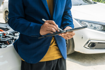 A businessman stands next to his damaged vehicle after an accident, holding a clipboard and...