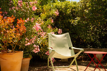 A light green garden chair and a round red garden table in the Mediterranean garden surrounded by...