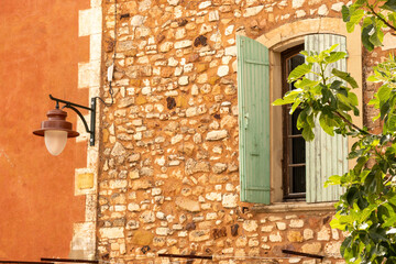 A view of a traditional house with brick wall and windows with green shutters in the ochre village...