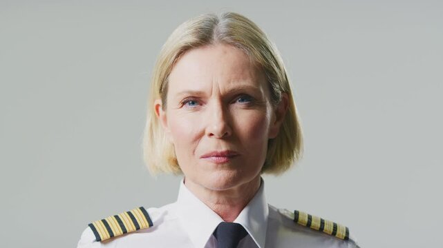 Serious mature female airline pilot or ship captain wearing uniform turning to face camera in front of plain studio background - shot in slow motion