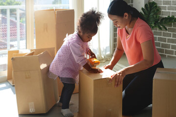 Mother teaches African daughter to stick tape on cardboard boxes at home, sticking adhesive tape on cardboard box