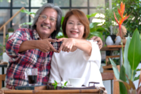 Senior couple spends their free time on the weekend tending flowers and taking care of each other in the green house, express Their love with the heart-shaped hand sign, selective focus