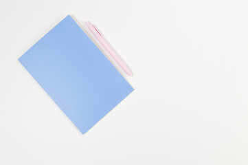 Top view of blue notebook, pink pen on white background. School, office wallpaper. Flat lay, copy space.