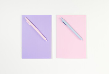 Top view of pink and purple notebooks, pink and blue pens on white background. School, office wallpaper. Flat lay, copy space.