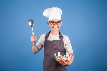 cheerful brunette boy cook in a chef's hat and apron prepares a salad. studio photo. My future profession concept