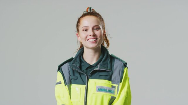 Smiling young female paramedic wearing uniform in front of plain studio background - shot in slow motion