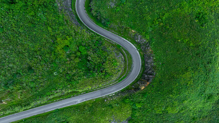 Aerial view road through the green forest on mountain road, Car drive on asphalt road going through green forest, Curved road from above.