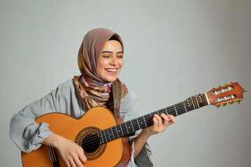 Fototapeta premium Musician in a hijab muslim girl splaying an acoustic guitar on white studio background. Dedication of kid learning music, musical education, talent development concept