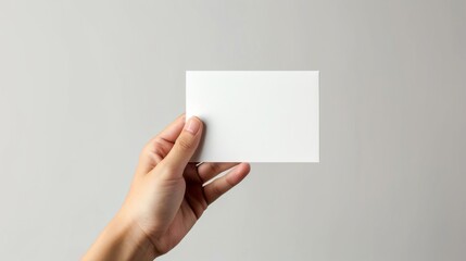 Obraz premium Hand holding blank white card against grey background, minimalistic concept