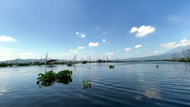 Rawa Pening lake contains water hyacinth plants against a backdrop of mountains and blue sky and white clouds