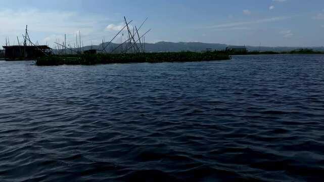 Rawa Pening lake contains water hyacinth plants against a backdrop of mountains and blue sky and white clouds
