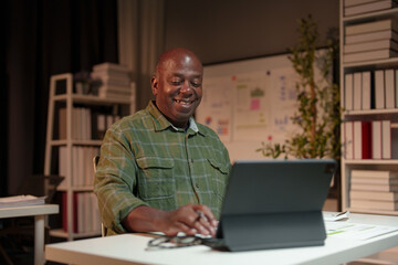 Happy African American man looking at laptop computer screen, typing, searching for information,...