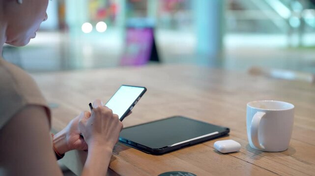 A woman is sitting at a table with a tablet and a cell phone in front of her
